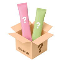 Clöud Café Mystery Sampler 2-piece set featuring two surprise instant drink stick packets in pink and sage green with question marks, emerging from an open kraft cardboard gift box branded with the Clöud Café logo