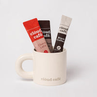 Clöud Café beige mug with rounded thick handle featuring Collagen Black Coffee, Collagen Hot Choco Zero, and Churro Latte sachets on a white background