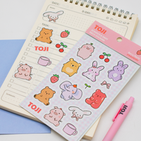Sheet of cute animal stickers with 'TOJI' branding on a notebook with a pink pen