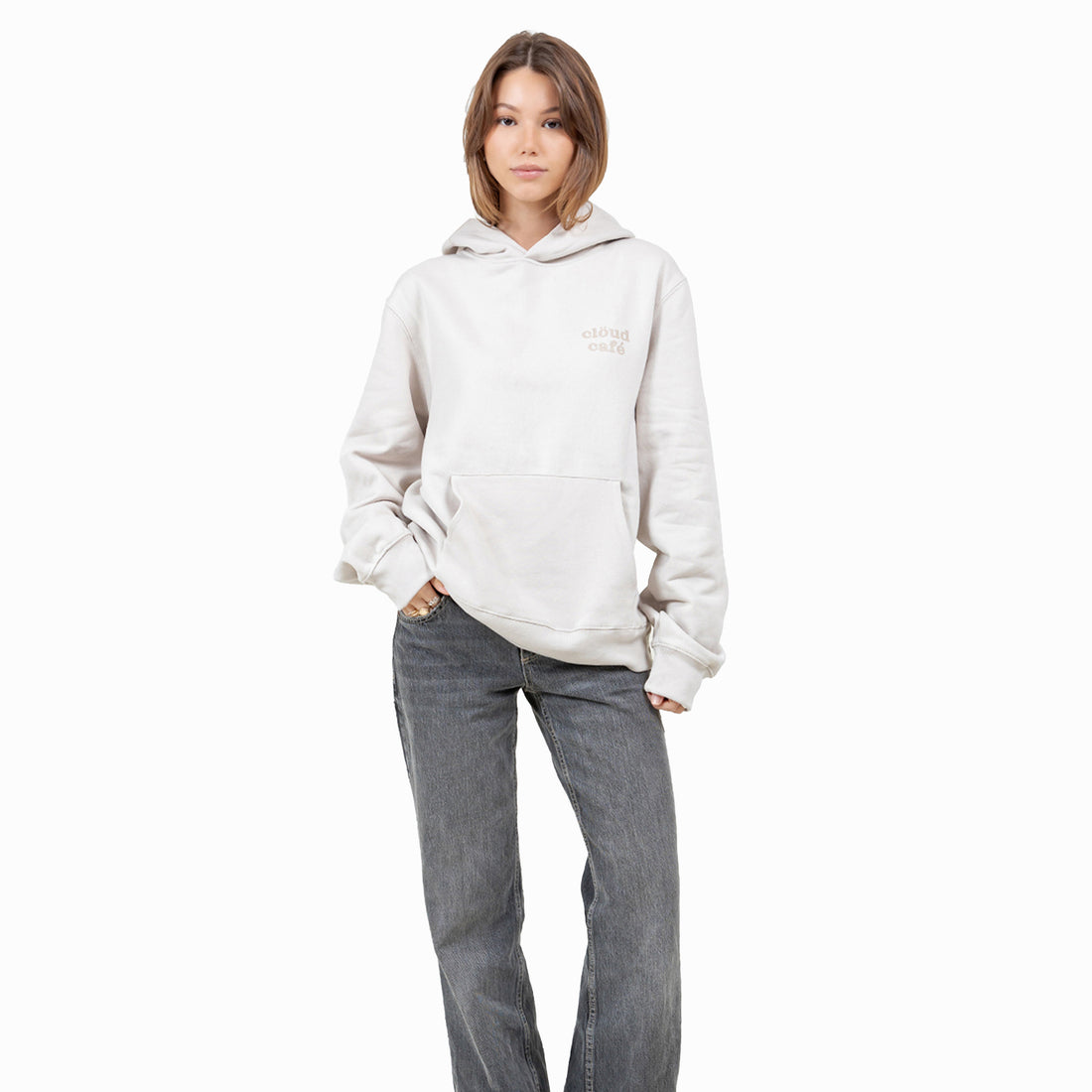 Full-body shot of model in light cream hoodie with clöud café logo and gray jeans.
