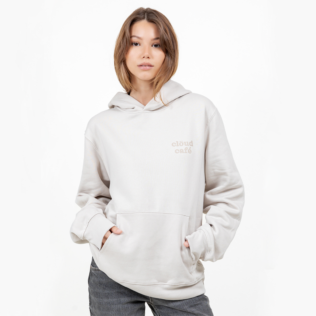 Model wearing light cream hoodie with minimal clöud café logo on the chest.