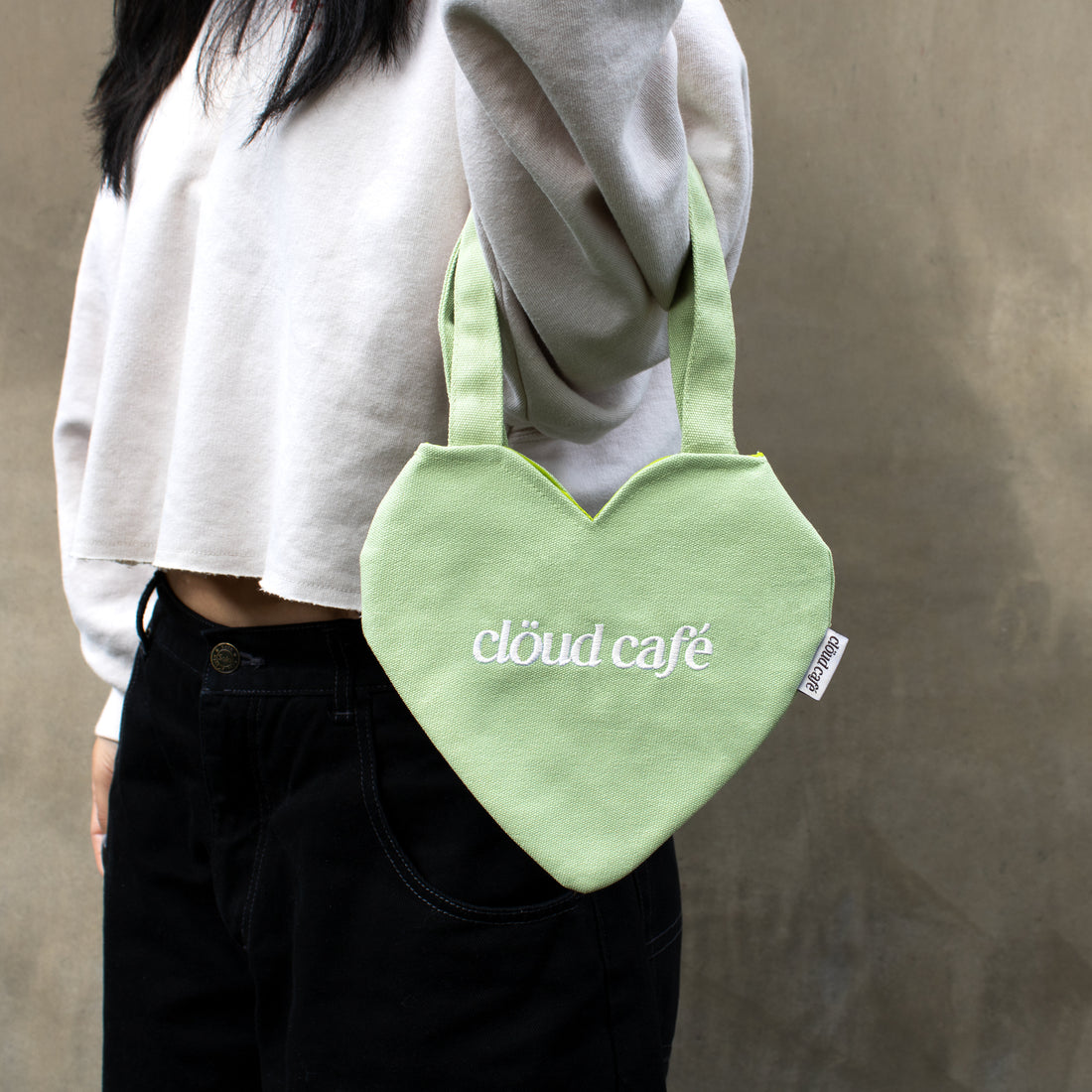 Light pastel green canvas mini heart tote bag with white embroidered logo.