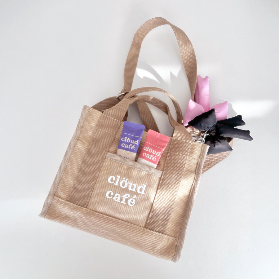 Light tan rectangle canvas tote bag with embroidered "Clöud Café" logo in white. Small pocket in front.  