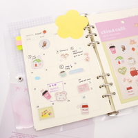 Open planner with decorative stickers and a yellow flower note on a light gray background. Image shows Cloud Cafe stickers on a journal.
