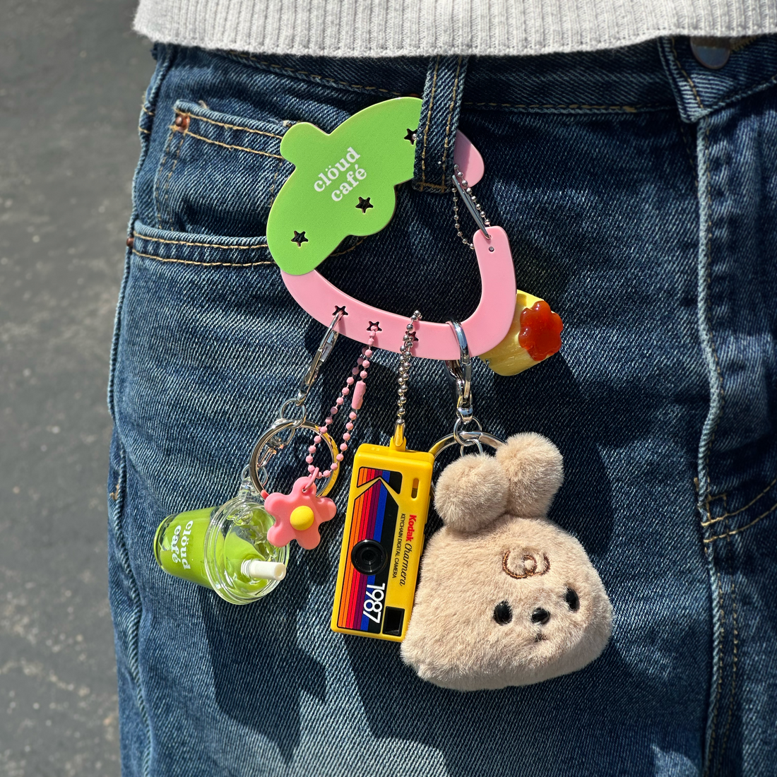 Strawberry Carabiner holding various charms, attached to jeans.