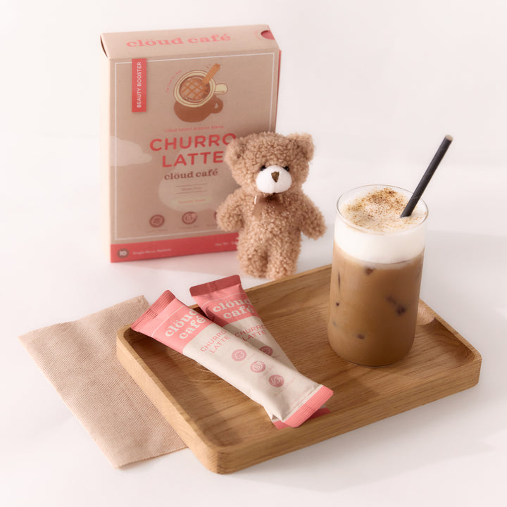 Creamy Churro Latte in a glass cup with straw, next to furry brown bear on a wooden tray.