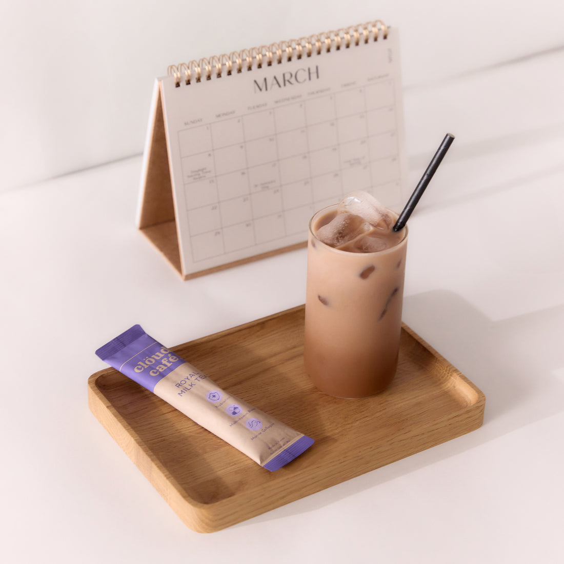 Royal milk tea sachet next to glass of Iced Royal Milk Tea with a straw on a wooden tray next to a March calendar.