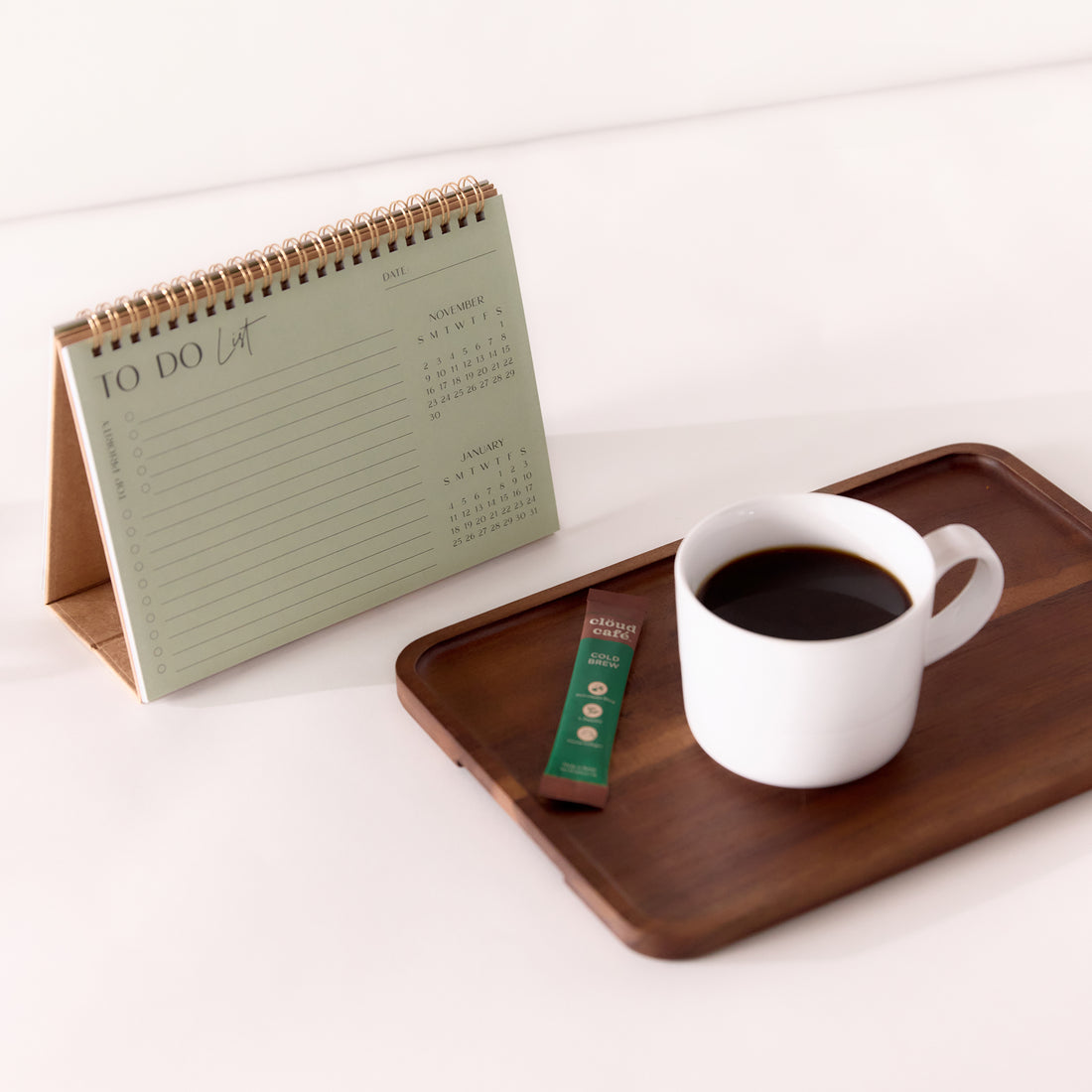 White cup of hot black coffee on dark wooden tray, next to standing calendar.