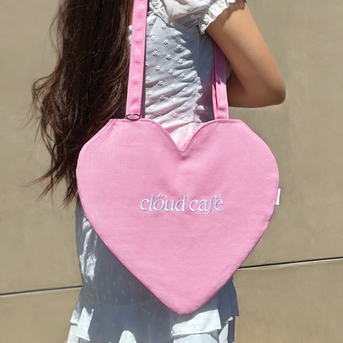 Clöud Café pink heart-shaped logo tote bag displayed in a lifestyle setting against a beige background