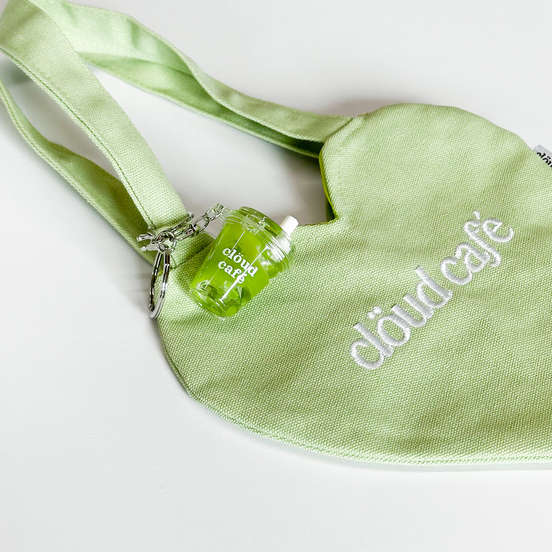 Clöud Café iced matcha shaker keychain hanging on a pastel green canvas tote bag.