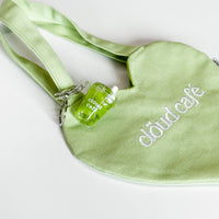 Clöud Café iced matcha shaker keychain hanging on a pastel green canvas tote bag.