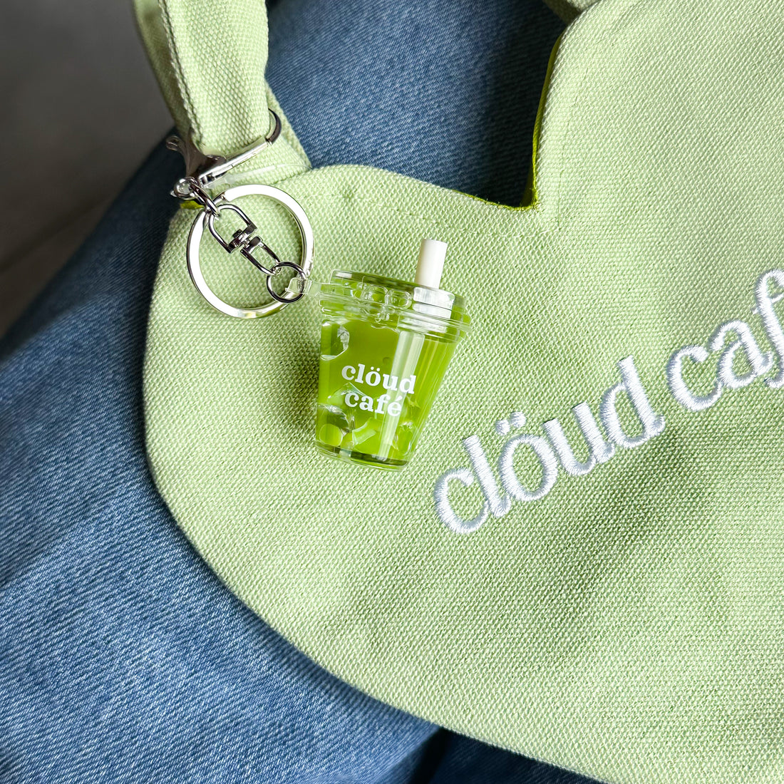 Clöud Café iced matcha shaker keychain hanging on a pastel green canvas tote bag.
