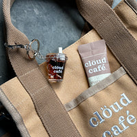 Clöud Café iced coffee shaker keychain hanging on a beige canvas tote bag.