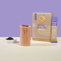 Iced milk tea in glass cup with black tea leaves next to it. Lavender background.