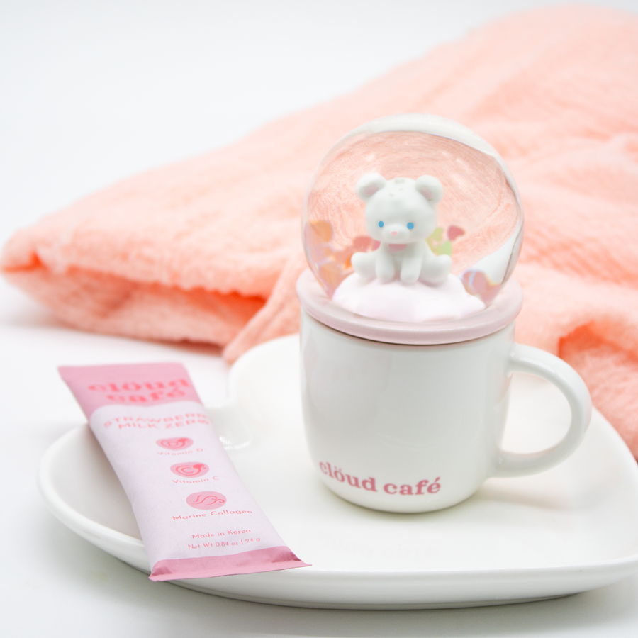 White Snow Glow Demitasse mug with white "cozy bear" inside pink accented snow globe topper placed beside strawberry milk zero sachet