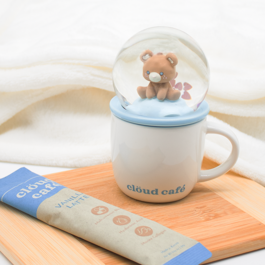 White Snow Glow Demitasse mug with brown "cozy bear" inside blue accented snow globe topper placed beside vanilla latte sachet