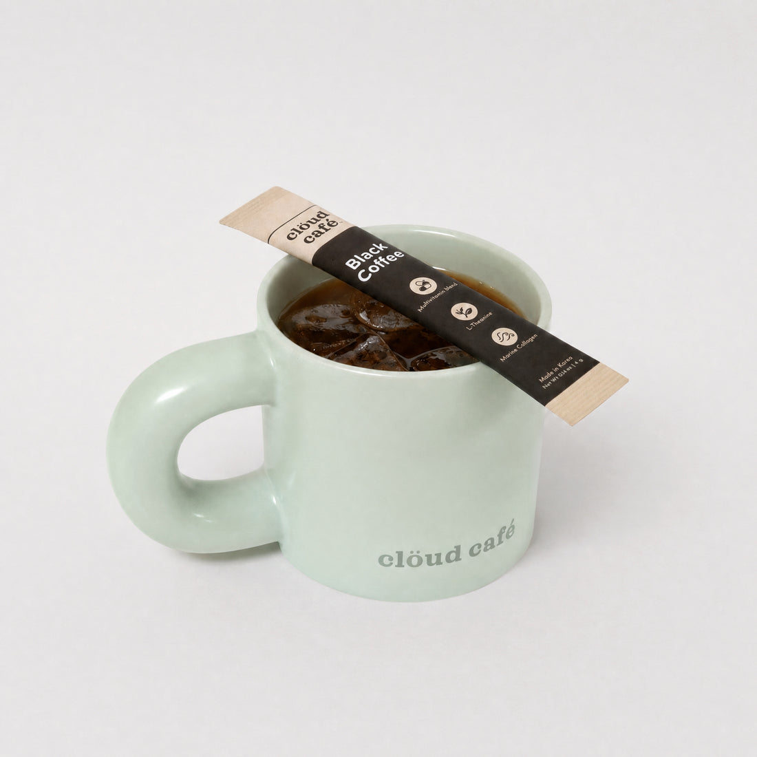 Clöud Café pastel green mug with a rounded thick handle against a white background featuring a Clöud Café Collagen Black Coffee sachet on top