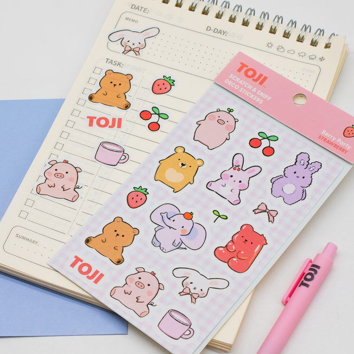 Sheet of cute animal stickers with 'TOJI' branding on a notebook with a pink pen