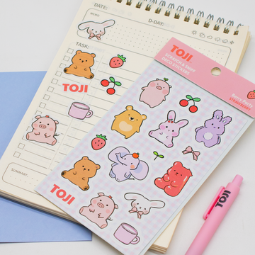 Sheet of cute animal stickers with 'TOJI' branding on a notebook with a pink pen