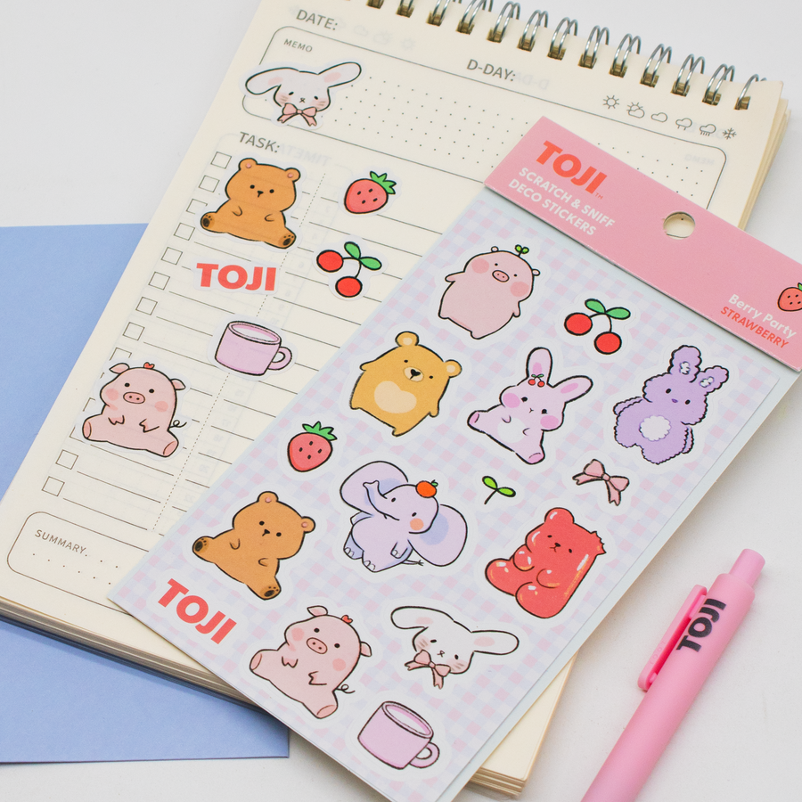 Sheet of cute animal stickers with 'TOJI' branding on a notebook with a pink pen